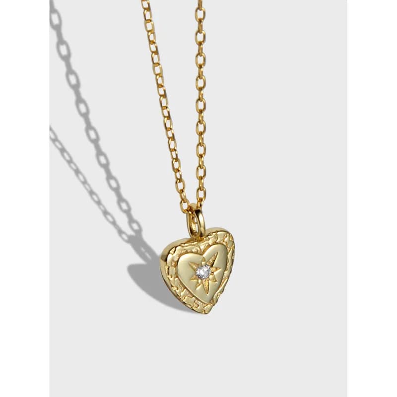 Polished silver heart pendant with textured border on a delicate chain, centered against a light background.