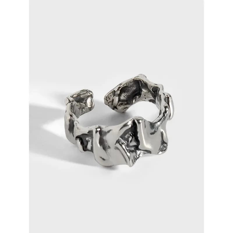 A matte sterling silver ring with an irregular, sculpted open band and organic facets sits on a white background.