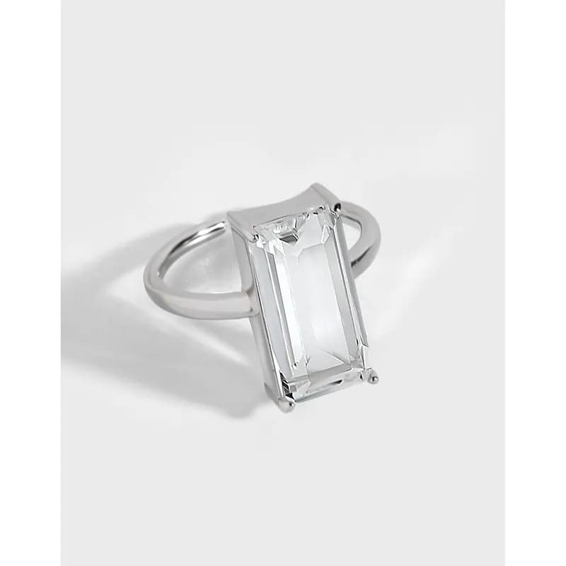 Polished sterling silver ring with a rectangular emerald-cut clear stone held by four prongs.