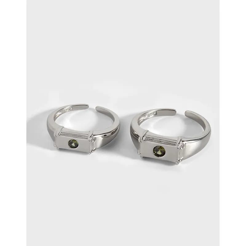 Two polished silver rings with rectangular front plates and small green stones on a white background.