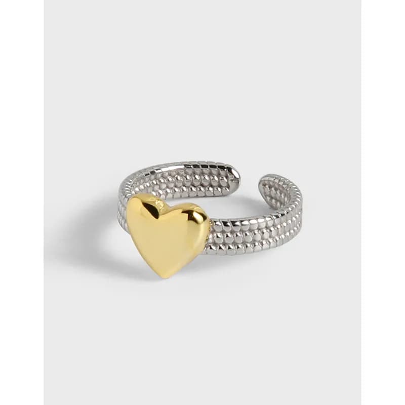 Open silver ring with a textured beaded band and a gold heart centerpiece in the foreground.