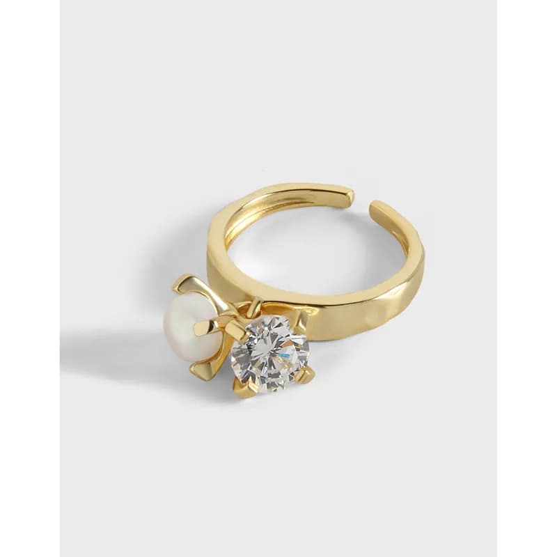 Gold-toned ring with a large clear gemstone and a small pearl detail on the side