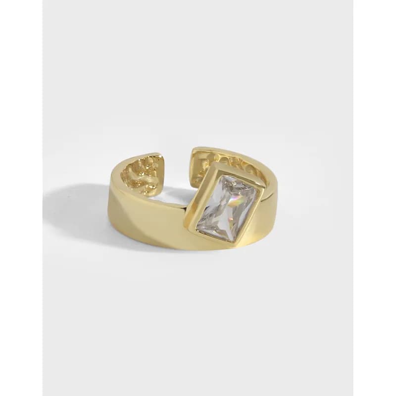 Polished sterling silver ring with a square-cut clear gemstone set in a bezel on a wide open band.