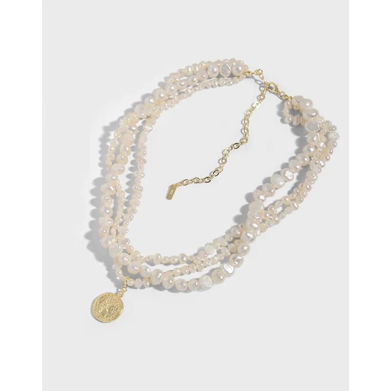 Three-strand pearl necklace with a gold coin pendant and adjustable clasp laid on a white background.