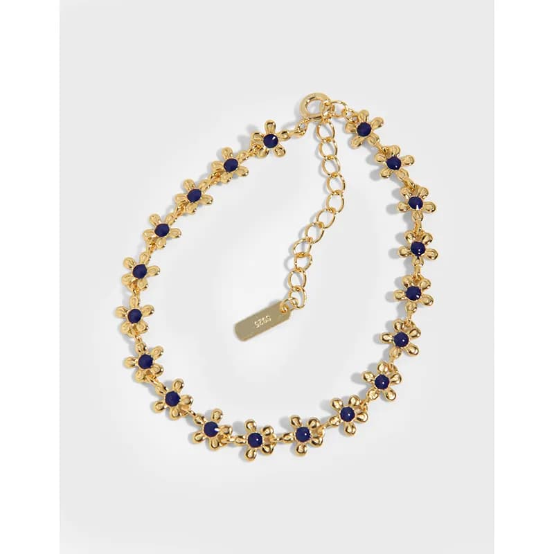 Polished sterling silver bracelet with small daisy motifs and blue centers laid in a gentle loop.