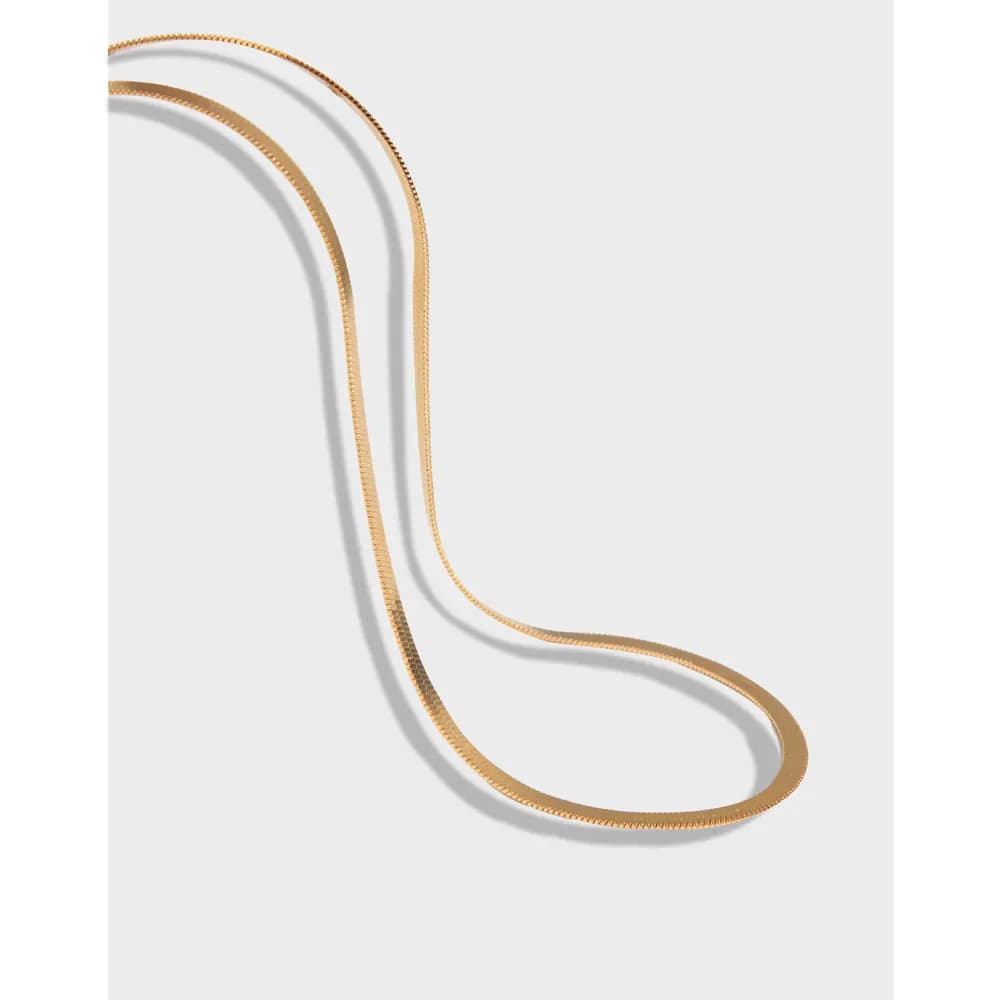 A polished sterling silver herringbone chain necklace laid out in a loose curve.