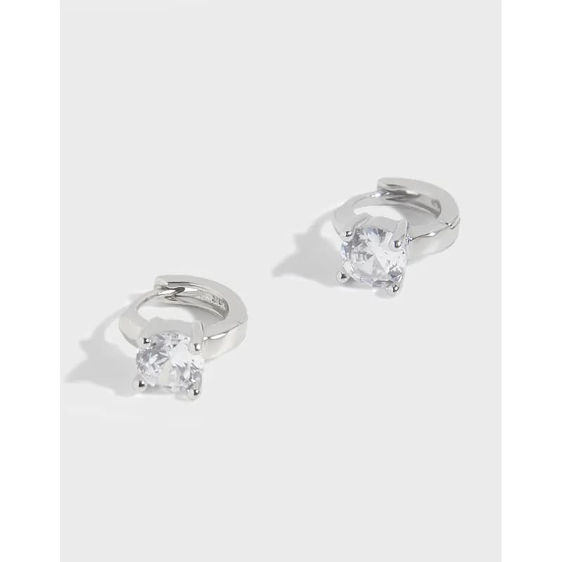 Two small polished sterling silver hoop earrings each with a prong-set clear round stone at the front.