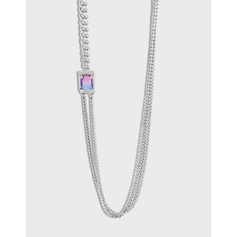 Close-up of a silver necklace with a square iridescent pendant hanging between two chains.