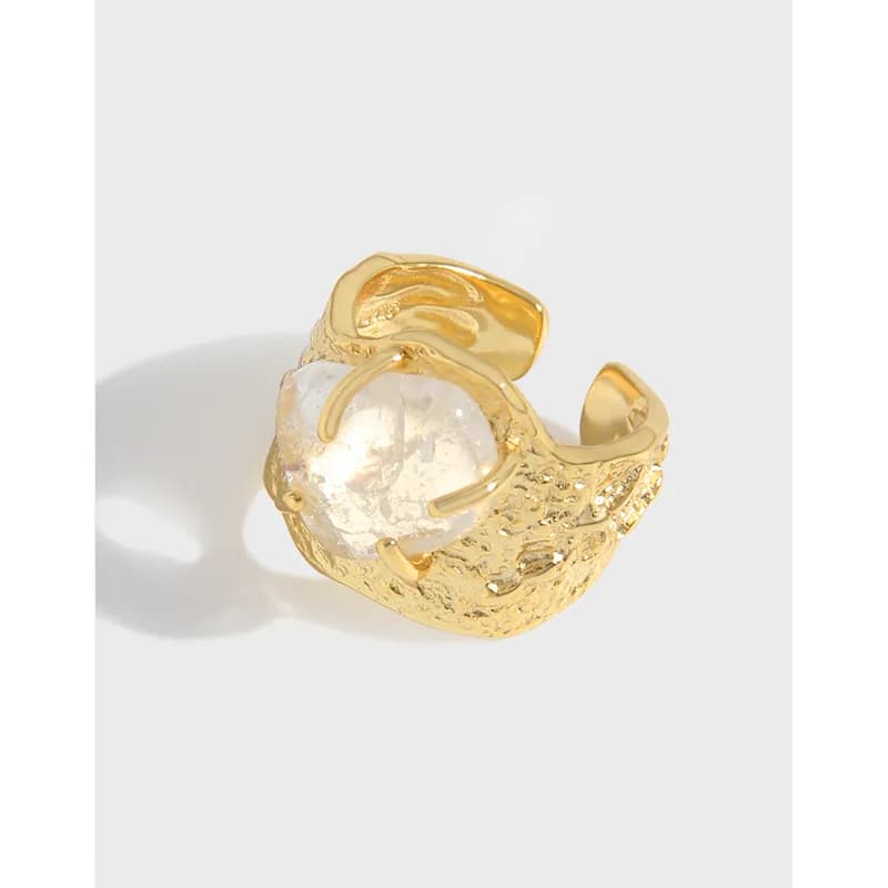 A textured gold-tone ring with a large faceted clear orb held by prongs on an open band.