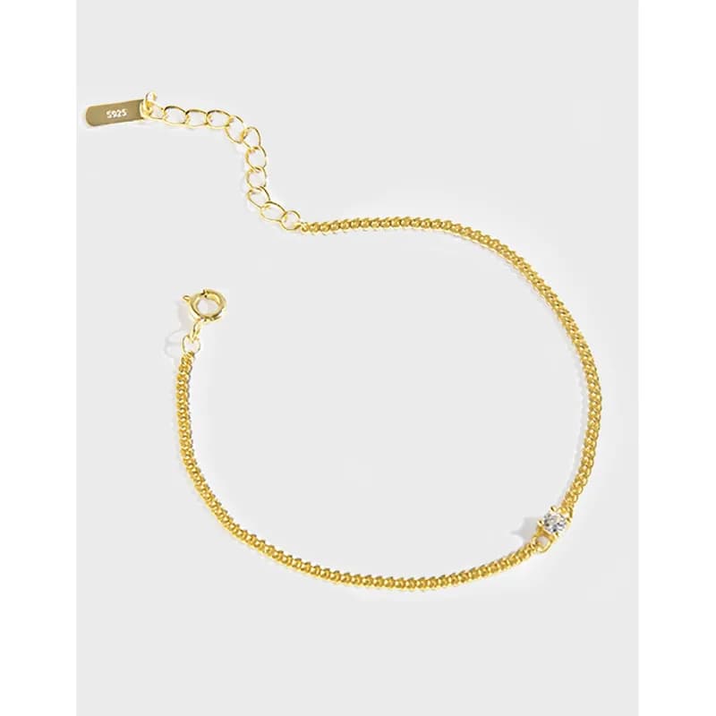 Polished gold-tone curb chain bracelet with an extender clasp and a small crystal accent near the end.