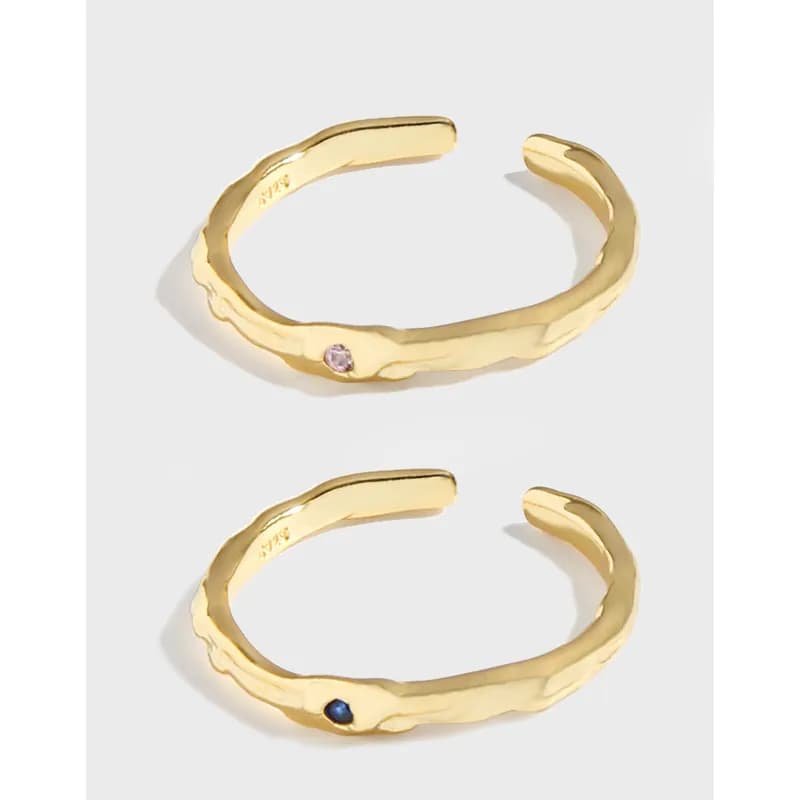Pair of hammered open rings in gold tone with small colored gemstones on a white background.