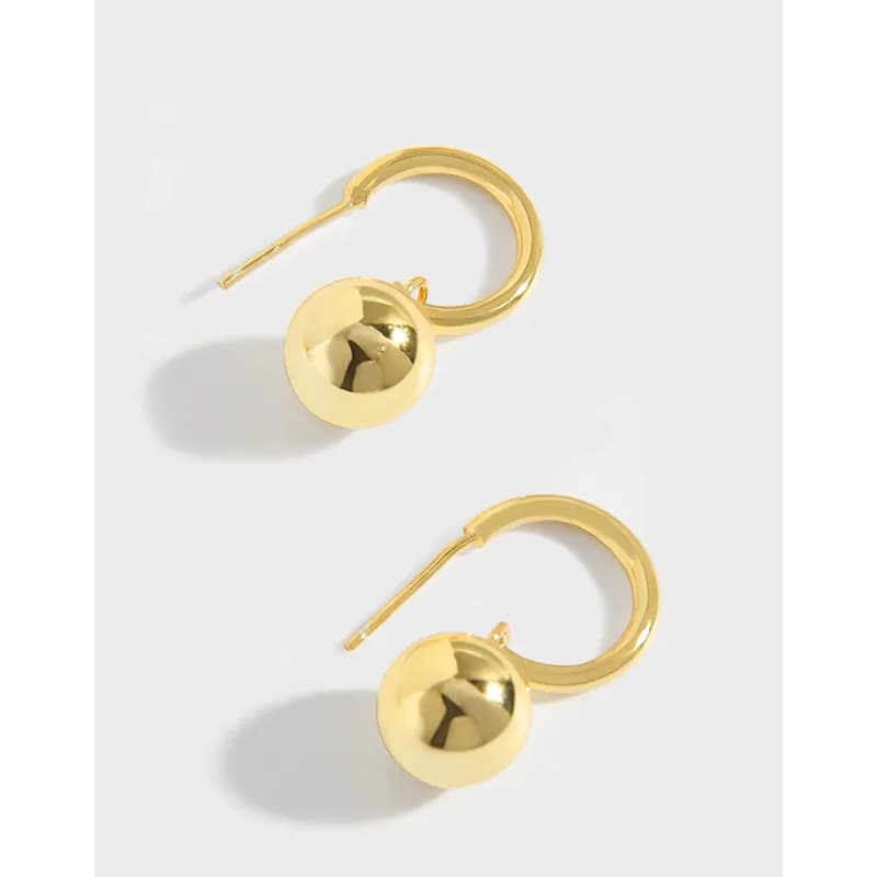 A pair of polished hoop earrings with a spherical ball charm on a light background.