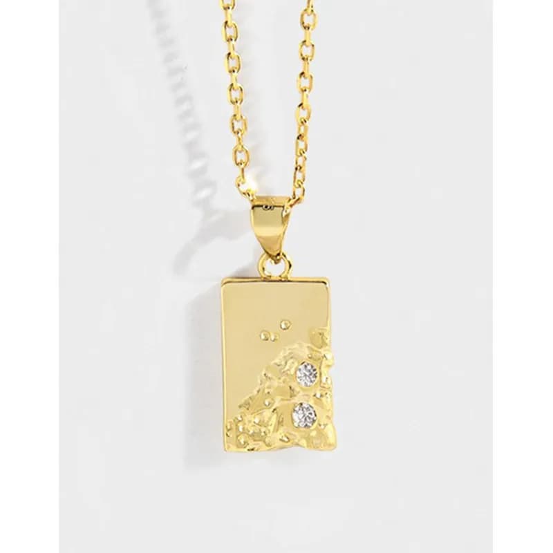 Gold-tone rectangular pendant with a textured lower motif and two small stones on a chain