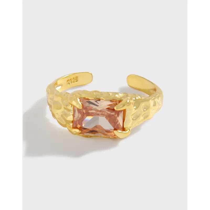 Polished gold-tone ring in a hammered texture with a rectangular peach gemstone set in claw prongs.
