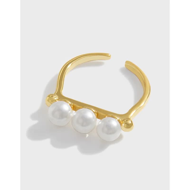 Open cuff ring with three white pearls along the front edge on a polished surface.