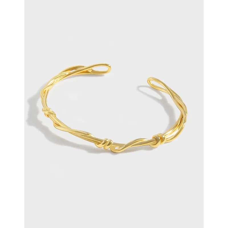 Gold-tone twisted rope cuff bracelet with knot details and open ends on a light background.