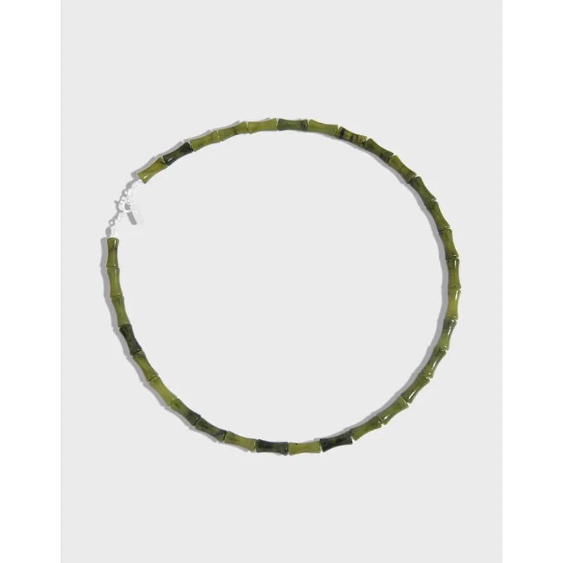 Polished sterling silver necklace with olive-green bamboo-like beads laid in a circular shape on a light background.