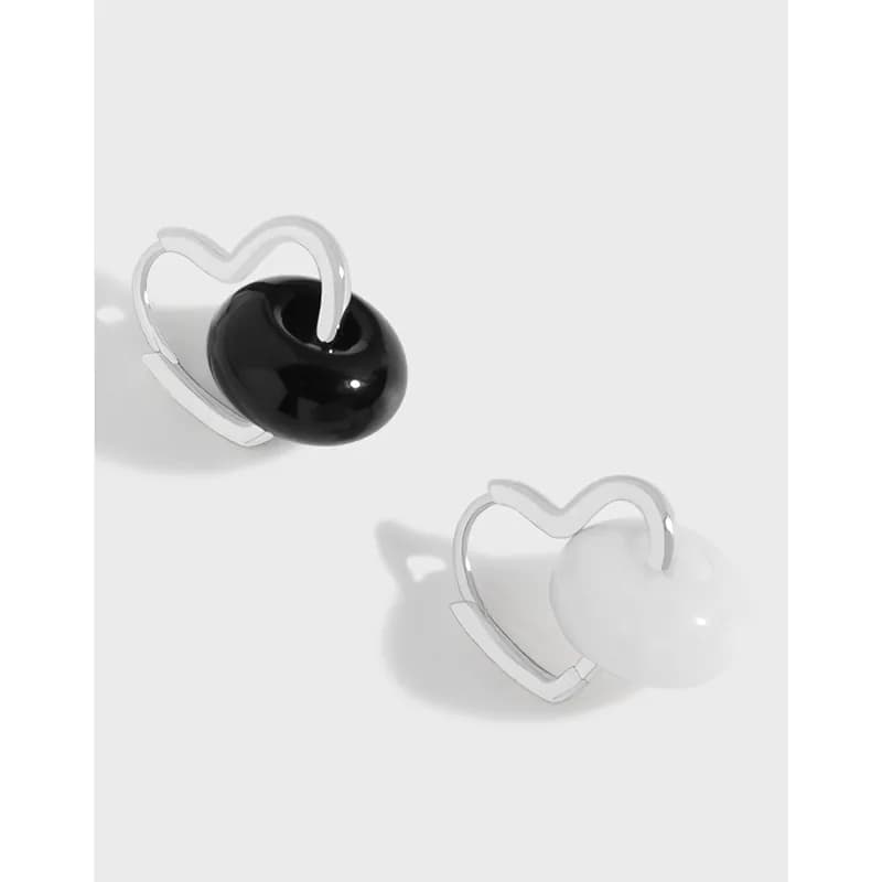 Two sterling silver heart-shaped hoop earrings, each with a pearl bead, one black and one white, shown on a light background.