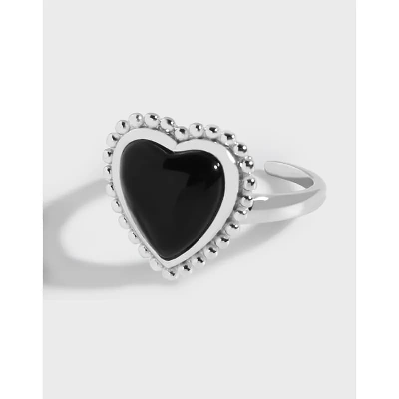 Sterling silver ring with a black heart centerpiece surrounded by a beaded halo on a pale background.