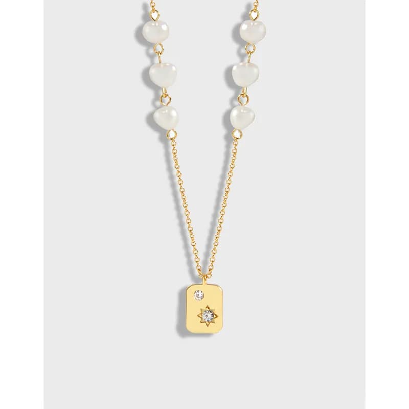 Close-up of a silver polished necklace with a beaded chain and a gold rectangular pendant with two stones.