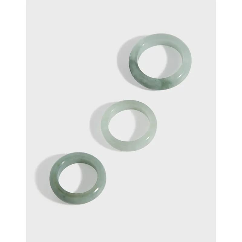 Three polished jade rings in varying pale greens arranged diagonally on a light background.