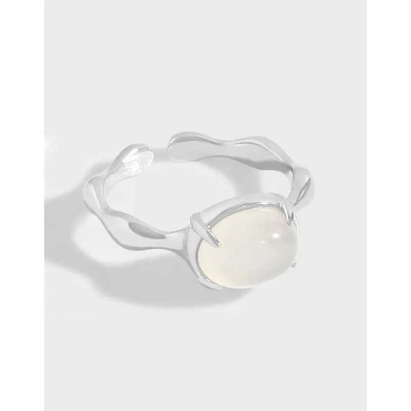 Polished silver ring with a round milky cabochon set in a four-prong bezel on a sculpted wavy band.