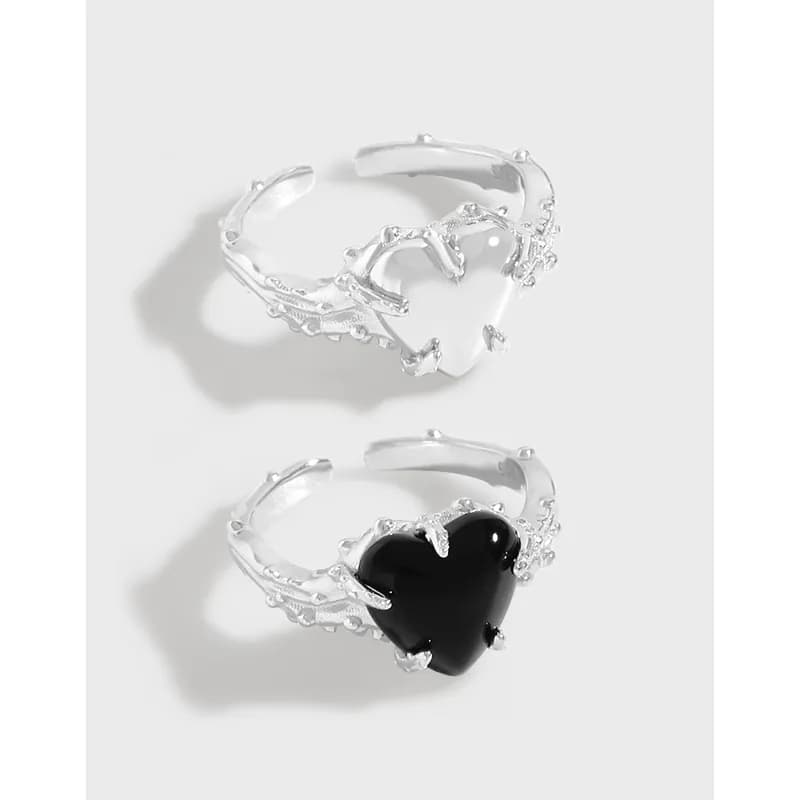 Two polished sterling silver rings with vine-like prongs, one featuring a black heart-shaped stone and the other a white stone.