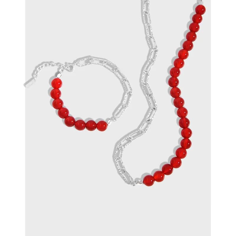 Silver chain necklace with red beads arranged along elongated link segments.