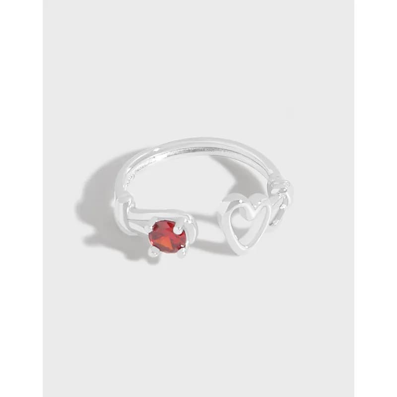 Polished silver open-wrap ring with a red gemstone and heart motif viewed from above.
