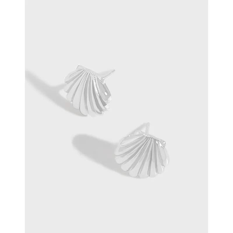 Polished sterling silver scallop shell earrings resting on a light surface, showing radiating ribbed design.