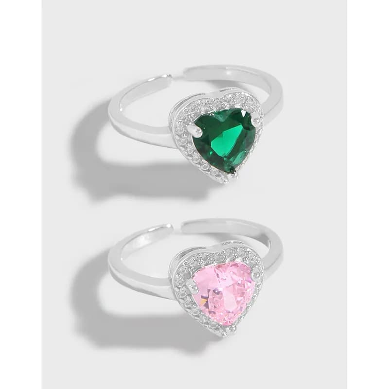 Two heart-shaped gemstone rings with pavé halos in emerald green and soft pink on polished silver bands.