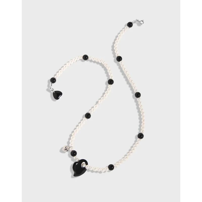 Polished pearl necklace with black bead spacers and a black heart pendant against a light background.