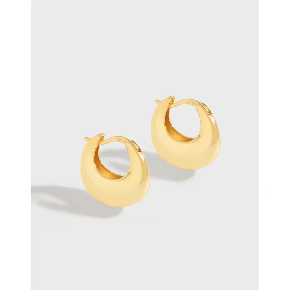 Polished gold-tone hoop earrings with thick curved bands and hinged clasps on a light background.