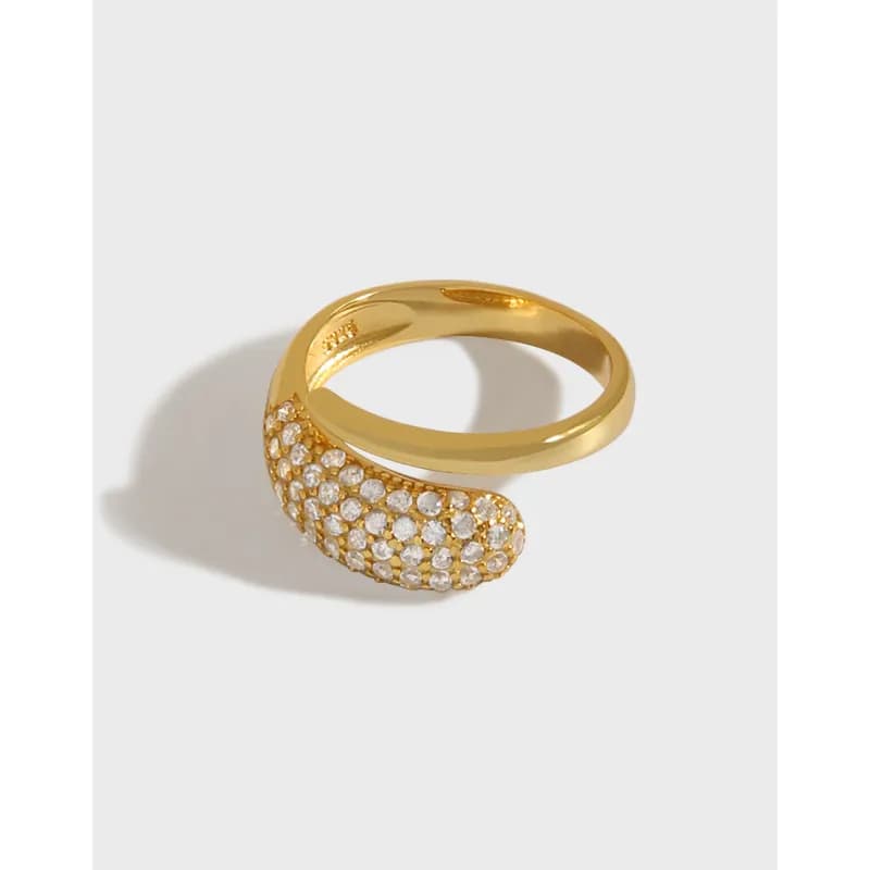 Gold-tone crescent pavé ring with a curved end resting on a light surface.
