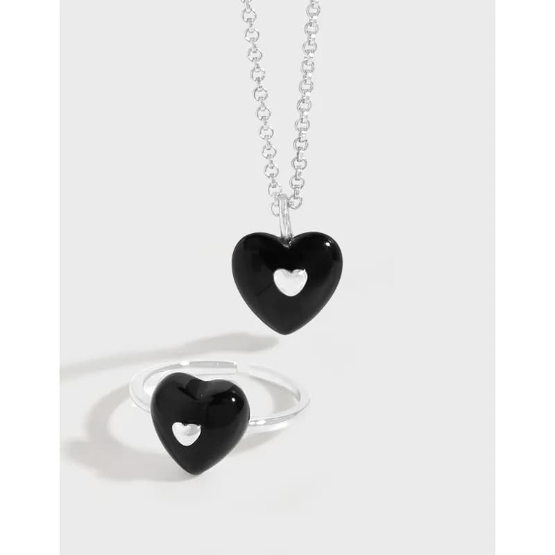 Polished sterling silver heart ring with a black enamel heart and silver heart cutout, shown beside a matching necklace in the hero image.