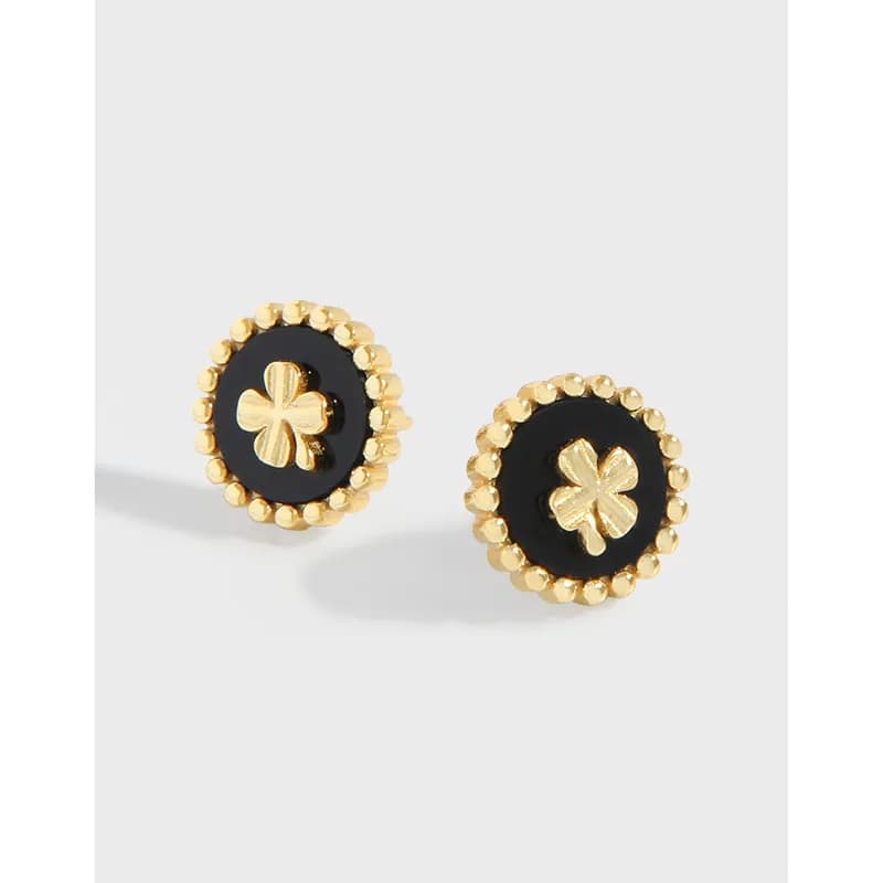 Circular stud earrings featuring black enamel, a gold beaded border, and a gold four-leaf clover center.