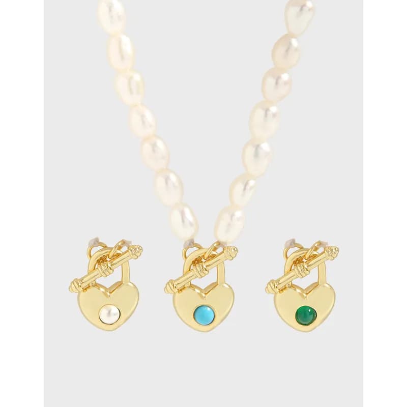 Pearl strand necklace with three gold heart pendants and colored cabochons on a light backdrop.