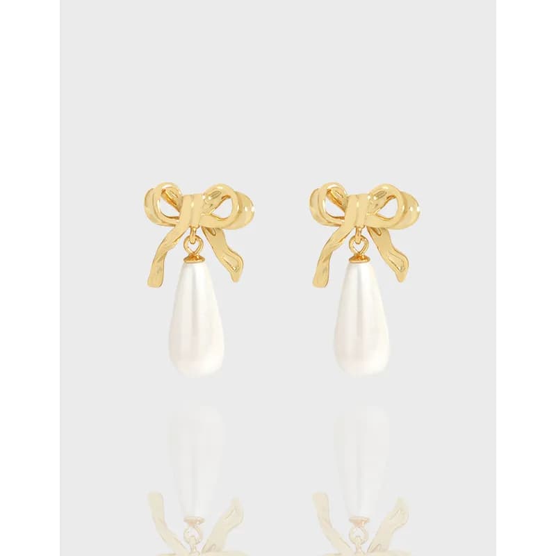 Polished sterling silver bow earrings with dangling white pearl drops on a light background.