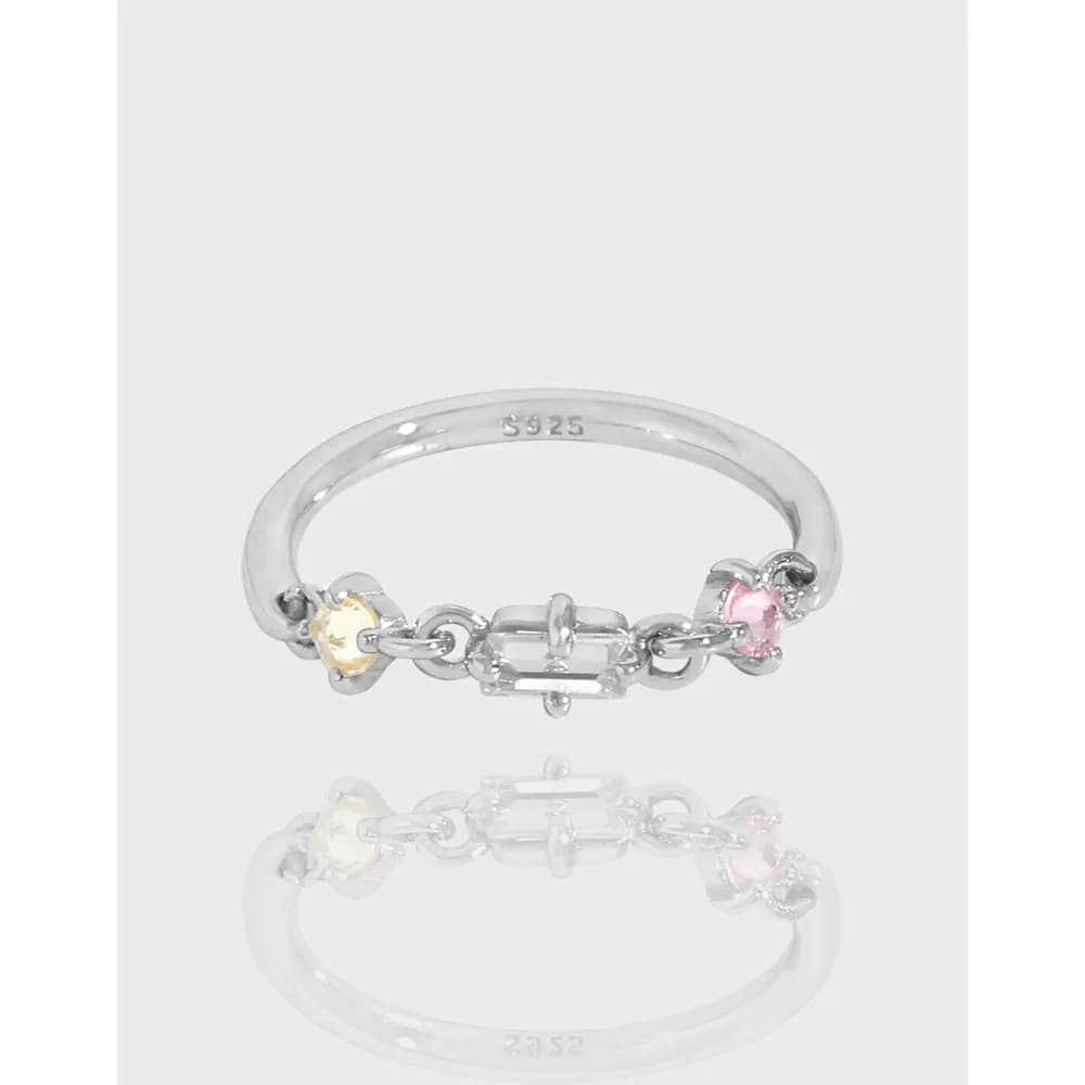 Polished silver chain-link ring with colored stones on the top, shown on a flat surface
