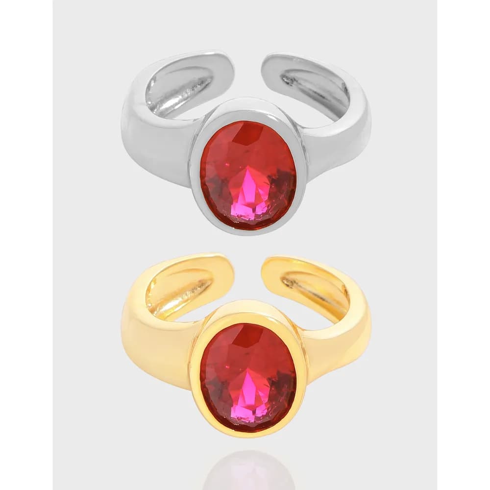 Open-band ring in silver and gold tones with a bezel-set oval red gemstone centerpiece.