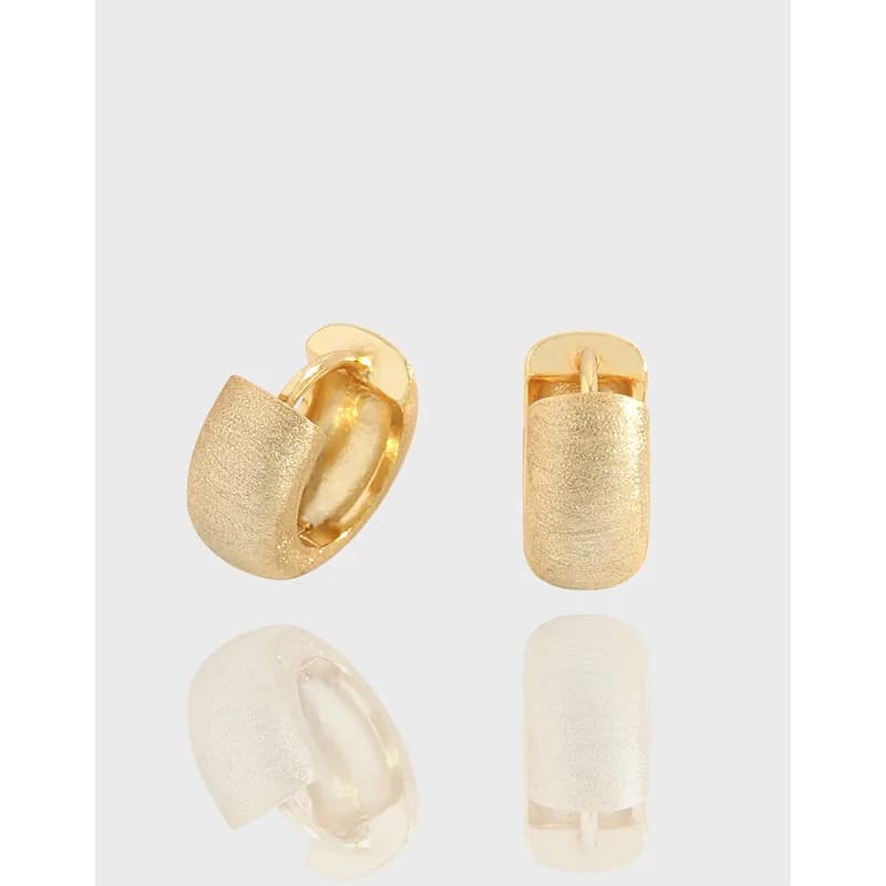 Gold-tone brushed huggie hoop earrings with a hinge closure in a close-up view.