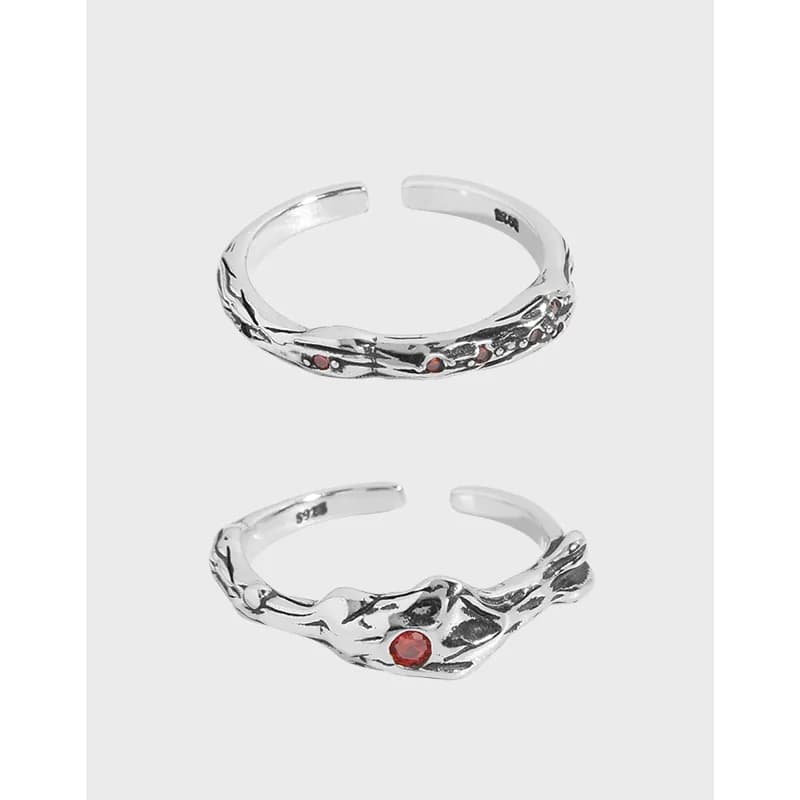 Polished sterling silver ring with vine-like texture and small red stones on a light background.