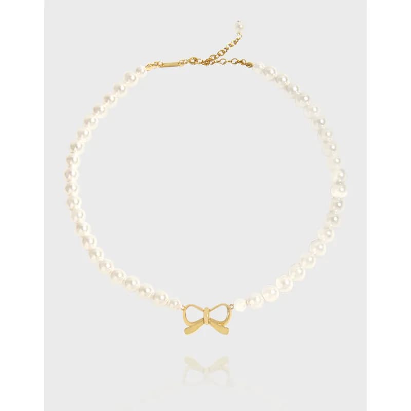 Pearl necklace with a small gold bow centerpiece on a polished strand against a light background.