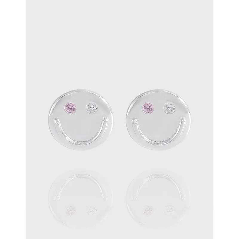 Polished sterling silver circular smiley face stud earrings with pink and clear gemstone eyes.