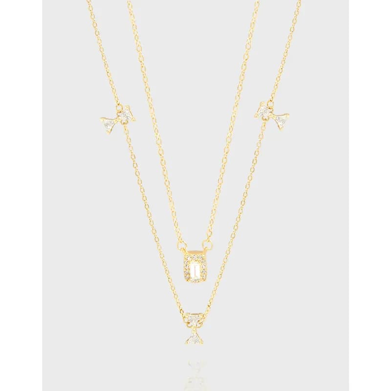 Three-layer necklace with two shorter chains and a longer chain, featuring bow charms and a rectangular pendant with stones.