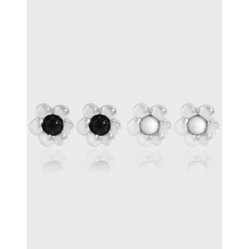 Row of four flower-shaped stud earrings with clear silver petals and black or white enamel centers.
