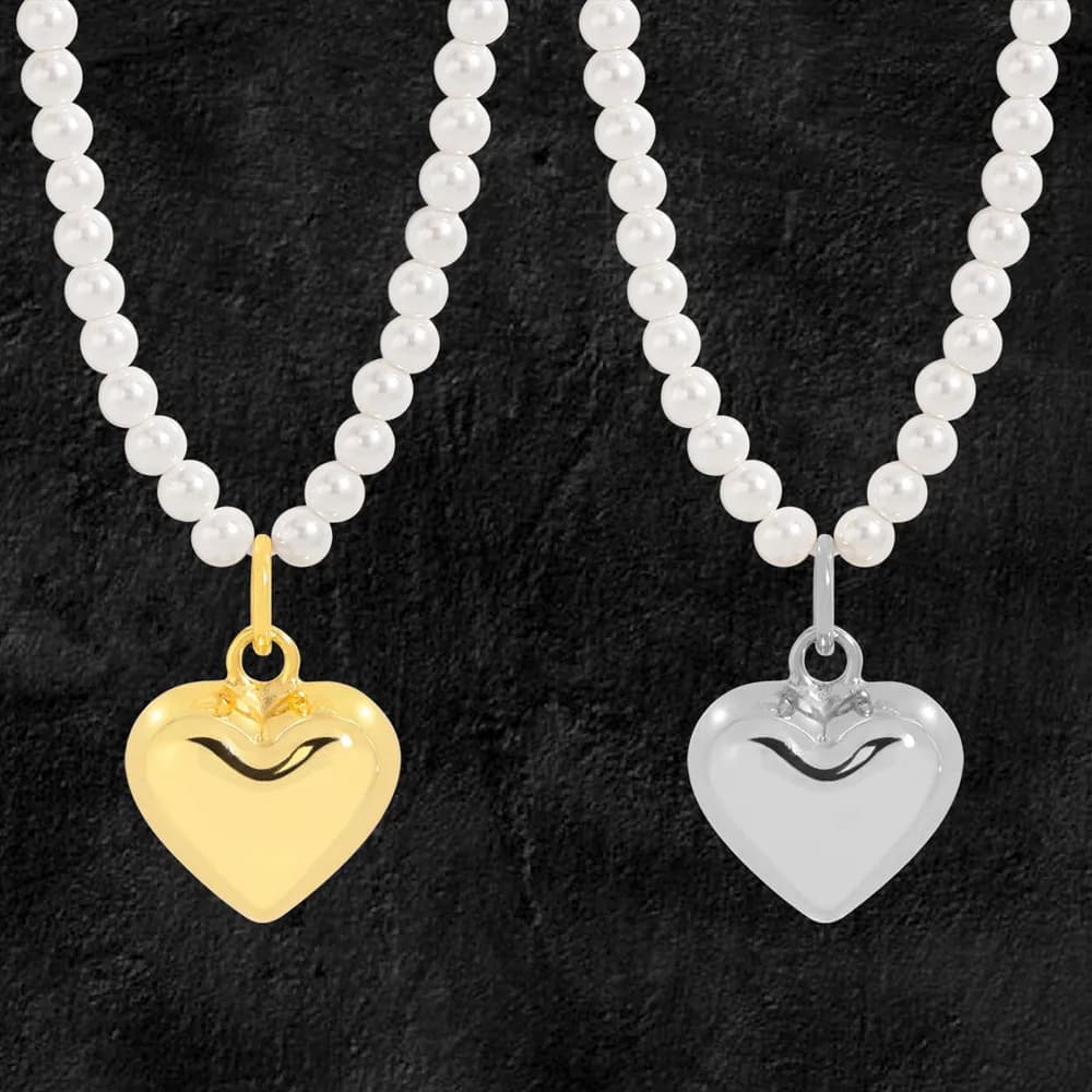 Two pearl bead necklaces with gold and silver heart pendants against a dark textured background.