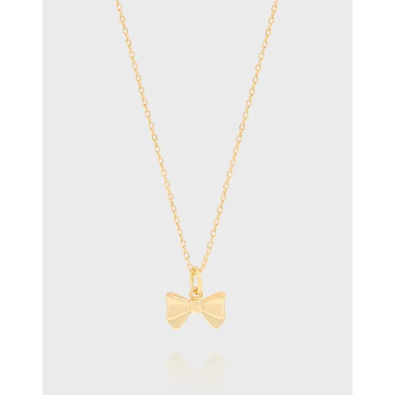 Delicate bow pendant necklace on a fine chain photographed against a pale background.