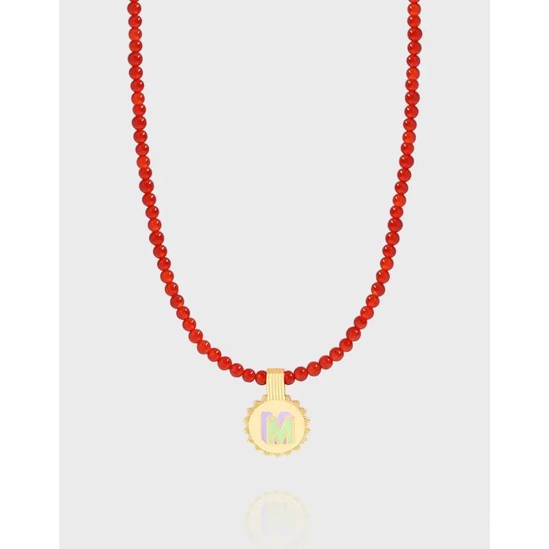 Red beaded sterling silver necklace with a gold-tone sunburst pendant featuring an iridescent M.