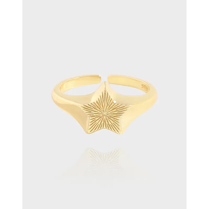 Polished gold-tone starburst ring with a raised textured star centerpiece on a slim band.